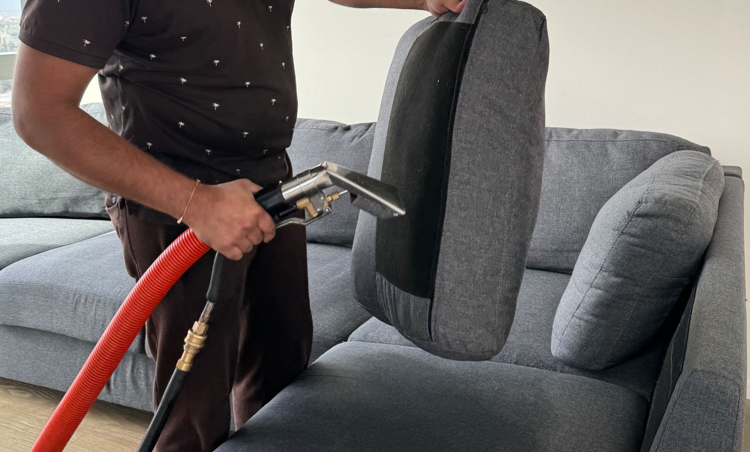 A person using a professional upholstery cleaning machine to deep-clean a grey sofa cushion inside a modern living room.