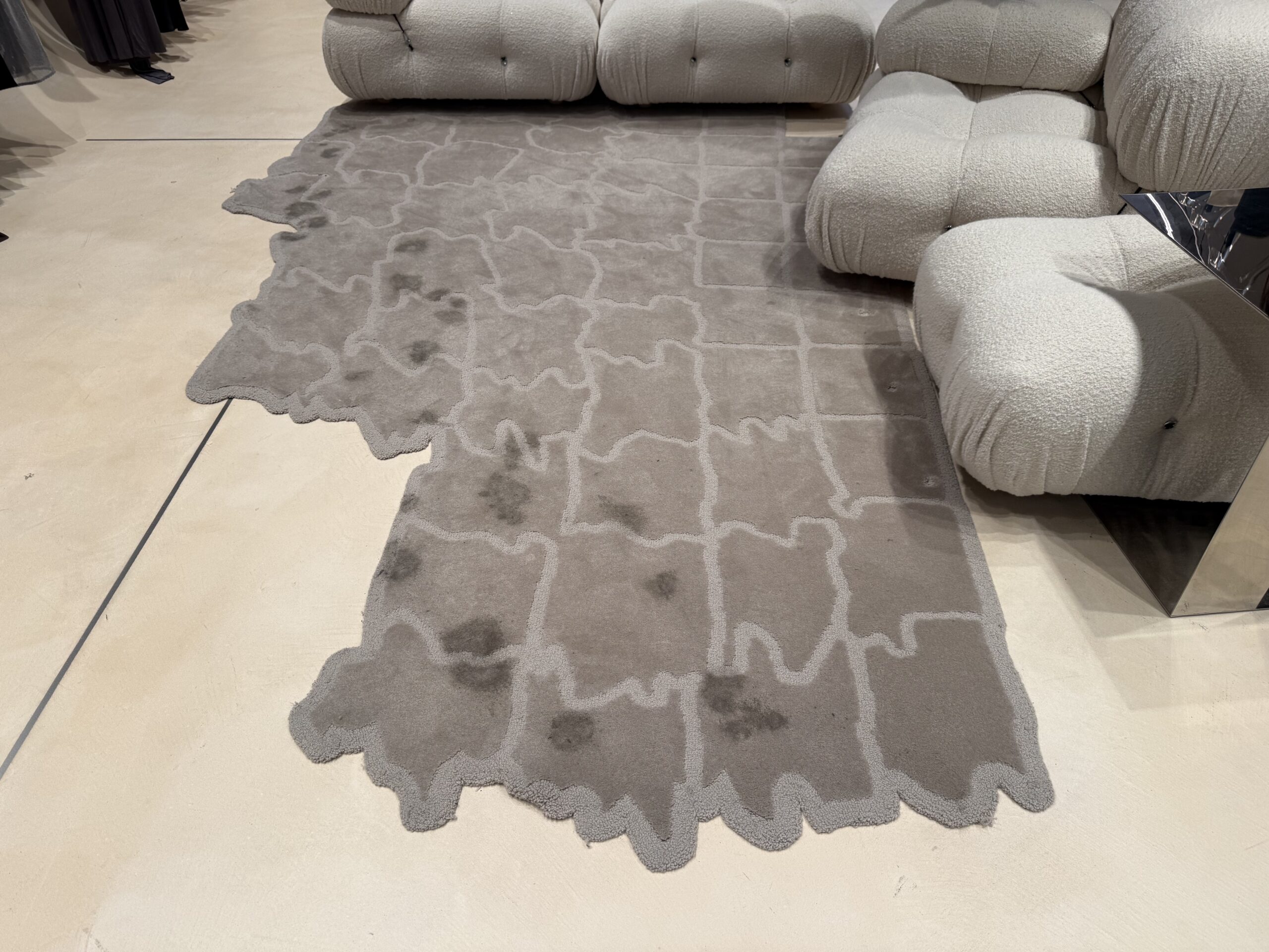 Large area rug with visible stains and foot traffic marks before professional cleaning.