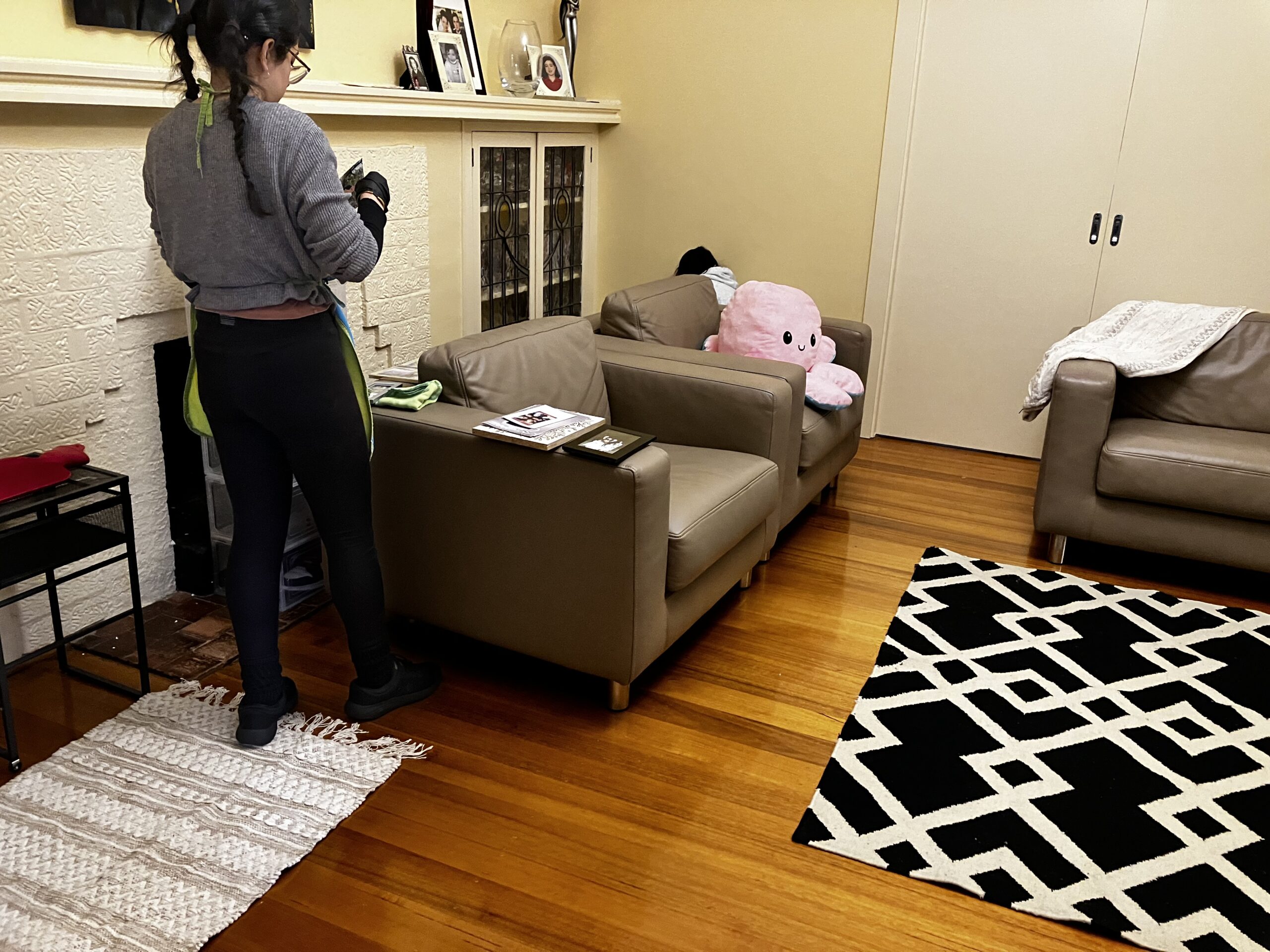 Professional cleaner wiping a fireplace area in a modern living room with sofas and wooden flooring.